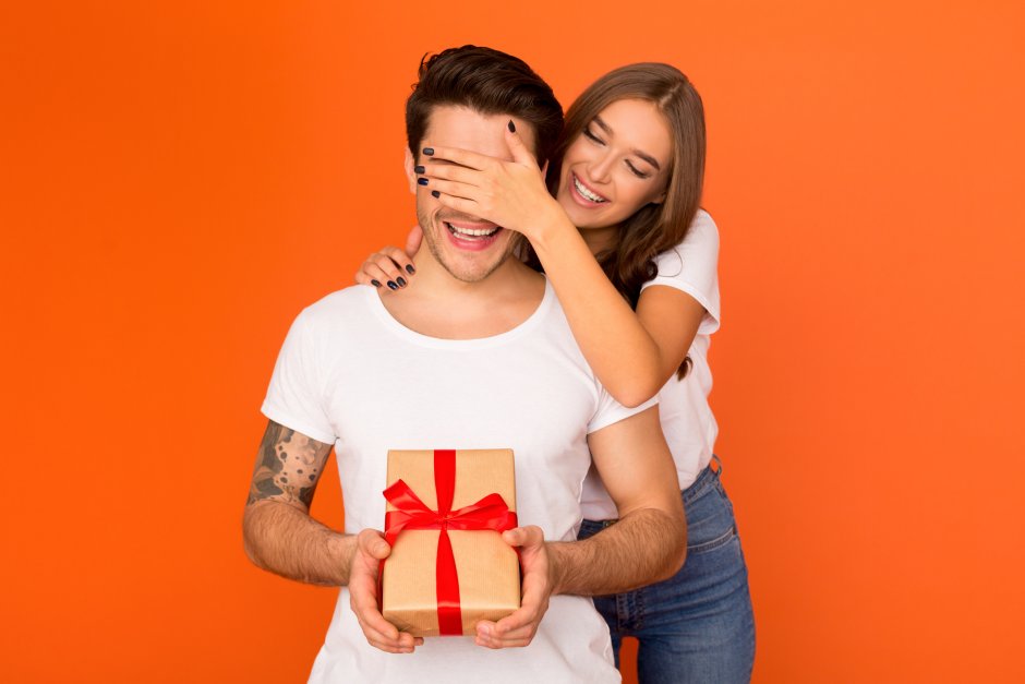 Женщина закрывает мужчине глаза и дарит подарок
